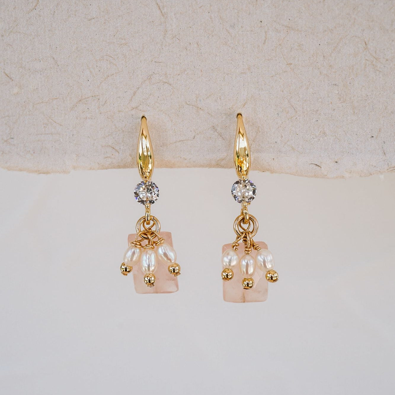 Gold earrings with pearl-like beads on a light background