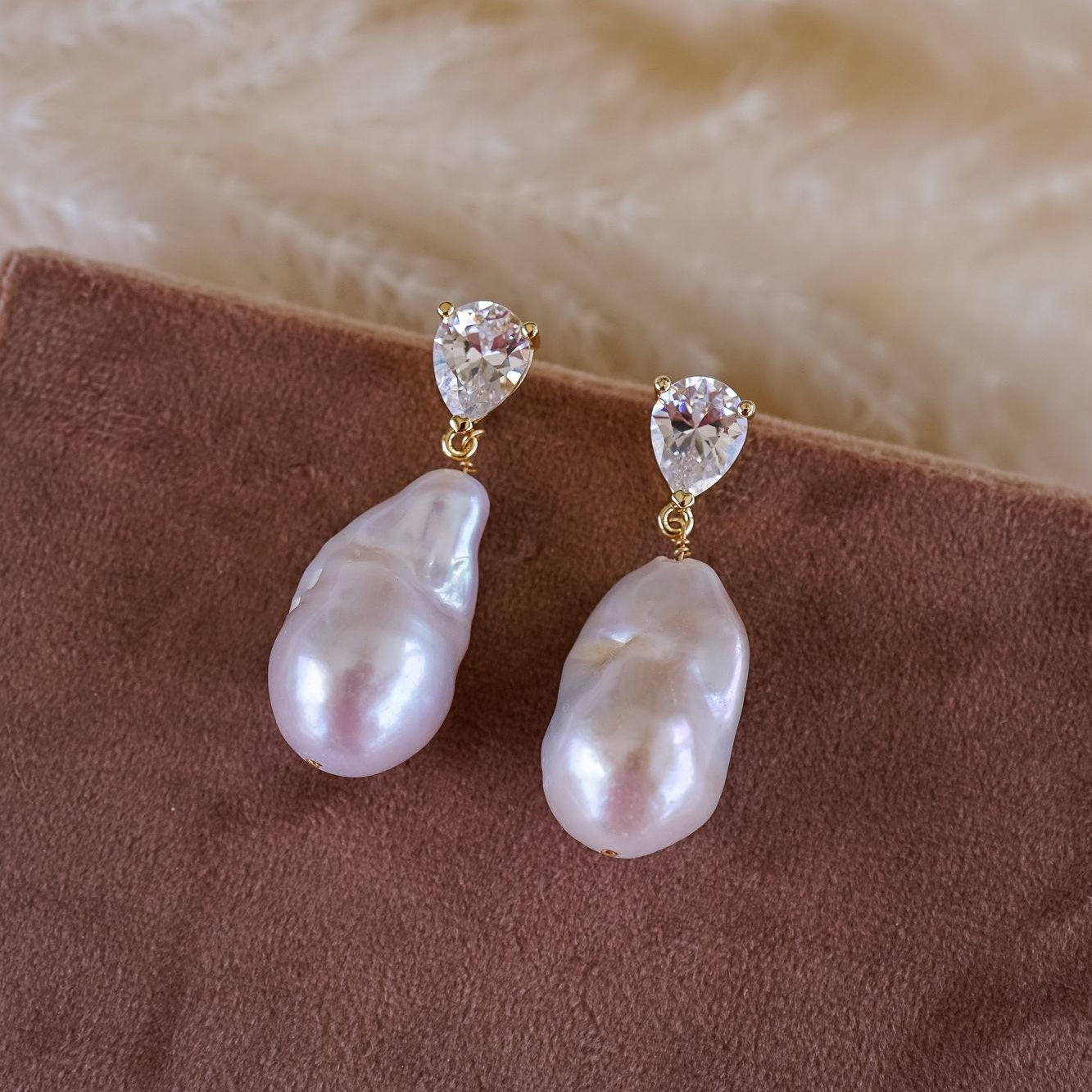 Pearl and crystal earrings on a brown surface with a beige fabric background