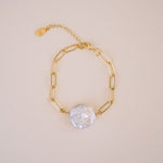 Gold chain bracelet with a pearl charm on a beige background
