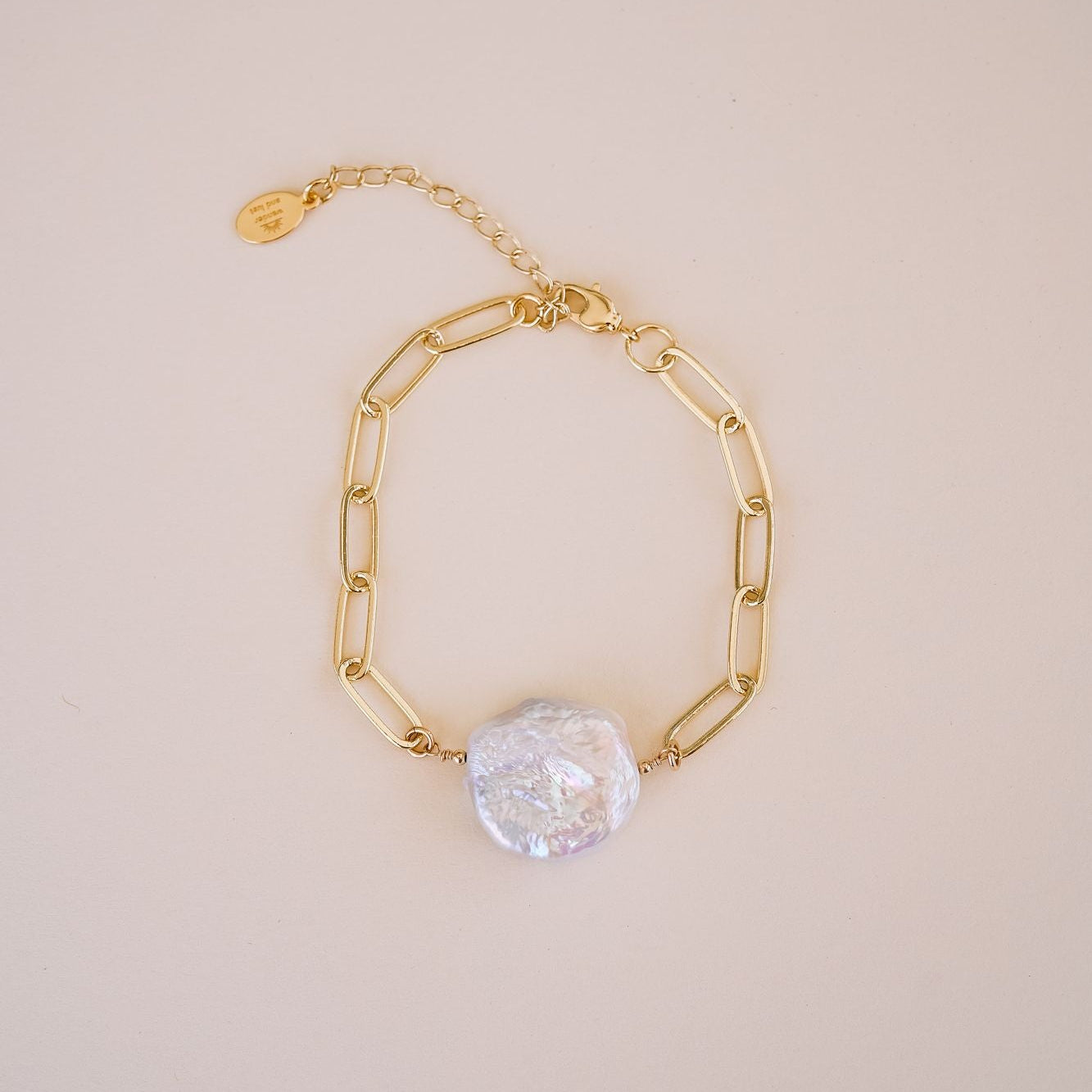 Gold chain bracelet with a pearl charm on a beige background