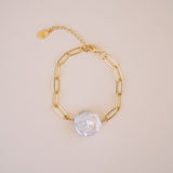 Gold chain bracelet with a pearl charm on a beige background