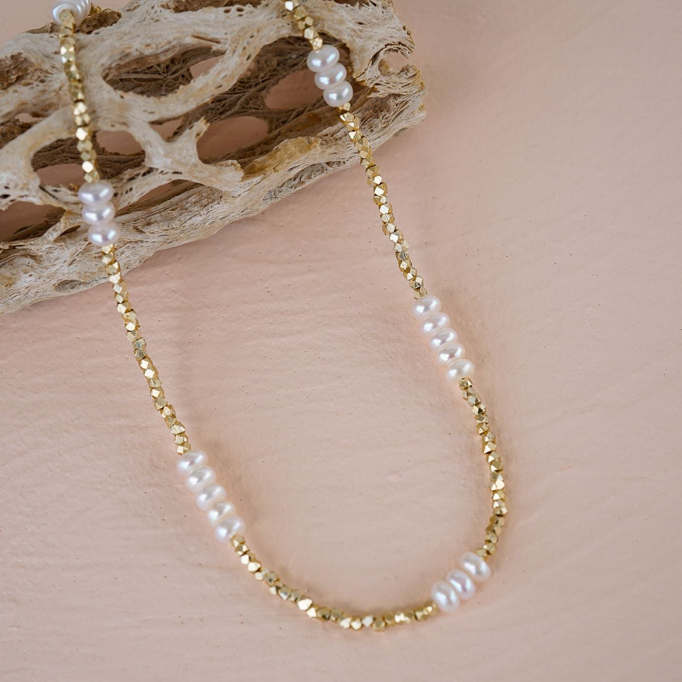 Gold and pearl beaded necklace on a textured beige surface