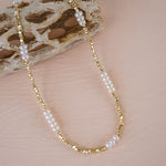 Gold and pearl beaded necklace on a textured beige surface
