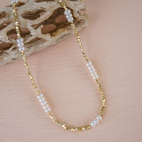 Gold and pearl beaded necklace on a textured beige surface