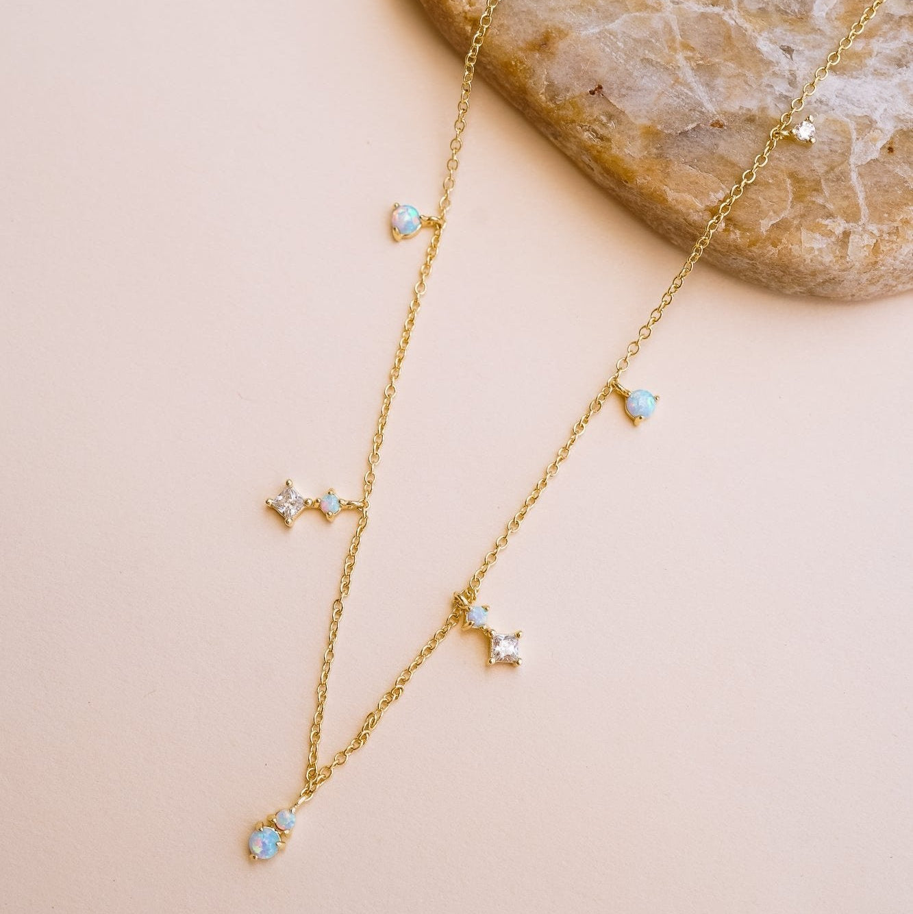 A 14k gold-plated brass necklace with delicate opal and cubic zirconia dangles, displayed against a neutral background.