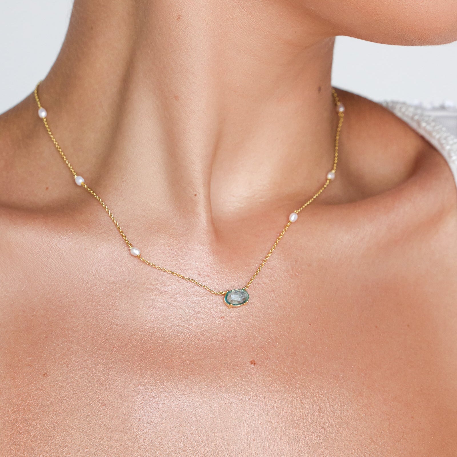 Gold something blue pearl necklace with a central gemstone on a person's neck against a neutral background