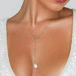 Pearl necklace with a blue gemstone worn by a person in a white lace garment.