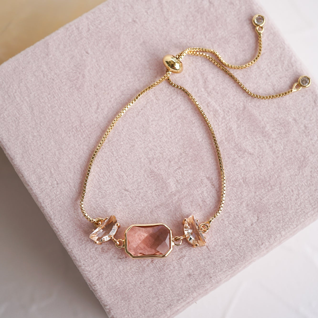 Gold bracelet with peach colored stone on a pink fabric background