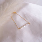 Gold bracelet with a bar pearl pendant on a white fabric background