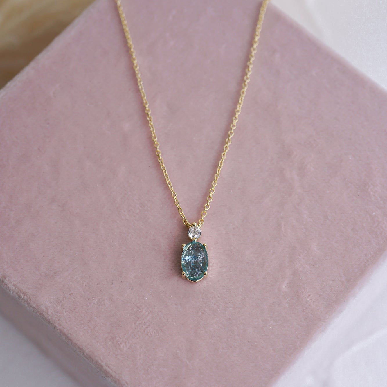 Gold necklace with a blue pendant on a pink stand