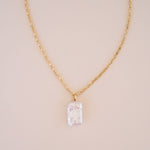 Gold necklace with a clear crystal pendant on a beige background