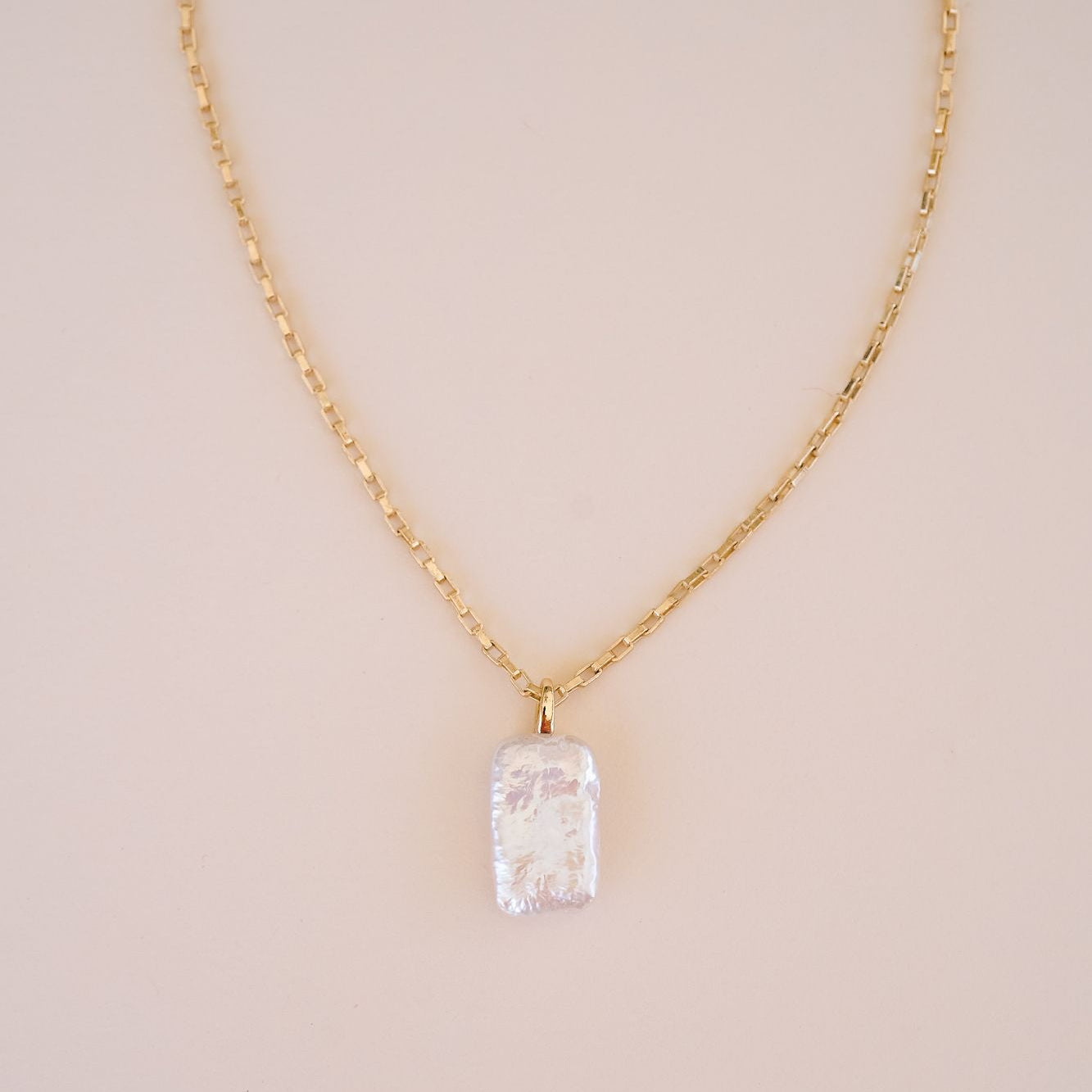 Gold necklace with a clear crystal pendant on a beige background