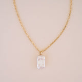 Gold necklace with a clear crystal pendant on a beige background
