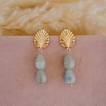 Gold earrings with blue green beads on a pink surface